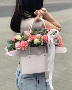 Цветочная композиция в переноске с гвоздиками и эустомой в руках девушки в другом ракурсе
